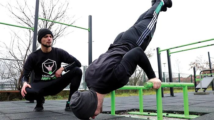 Ivan performing a handstand push-up on parallettes while Miko coaches, showcasing Calisthenics Ireland personal training in action