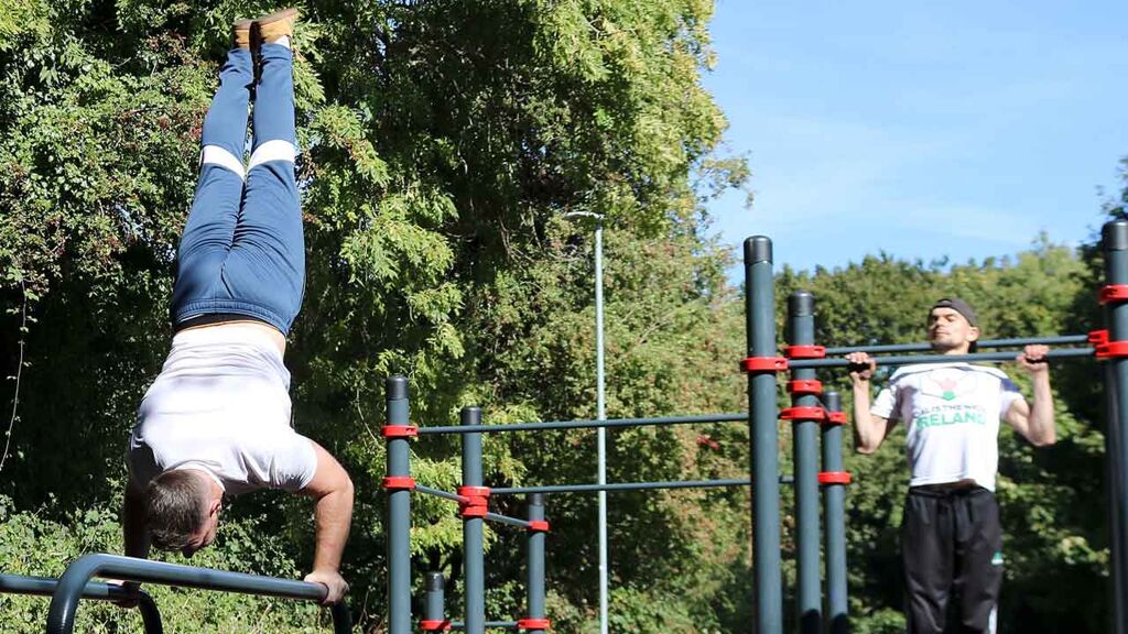 Calisthenics Ireland coaches performing pull-ups and handstand push-ups in a public park