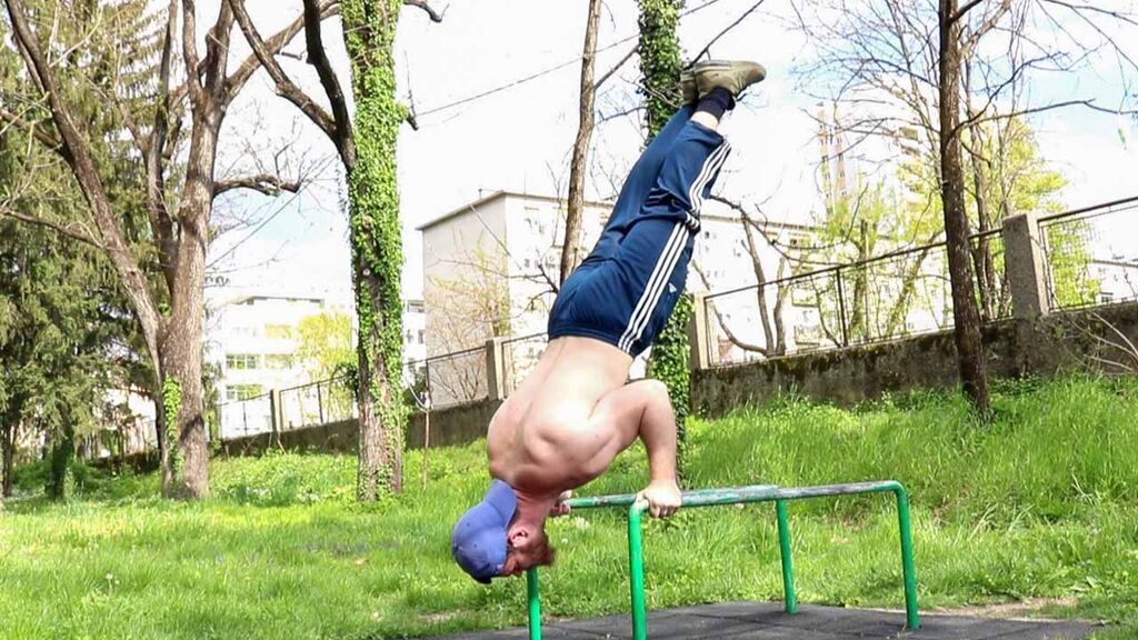 Calisthenics Ireland coach executing a handstand push-up on parallettes in a park, illustrating strength and body composition improvements