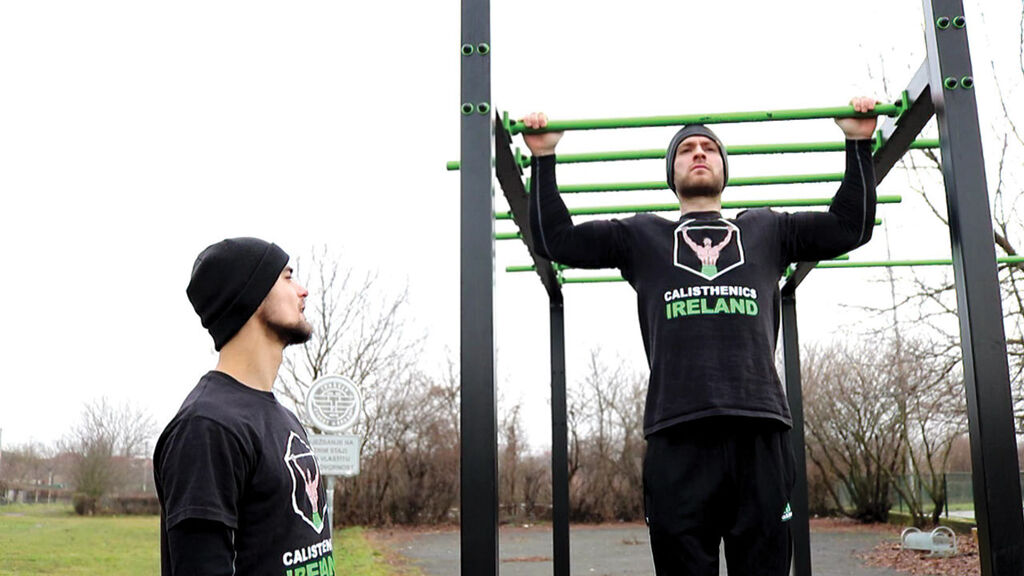 Calisthenics Ireland coach performing pull-ups outdoors in winter wearing layered clothing for cold weather training