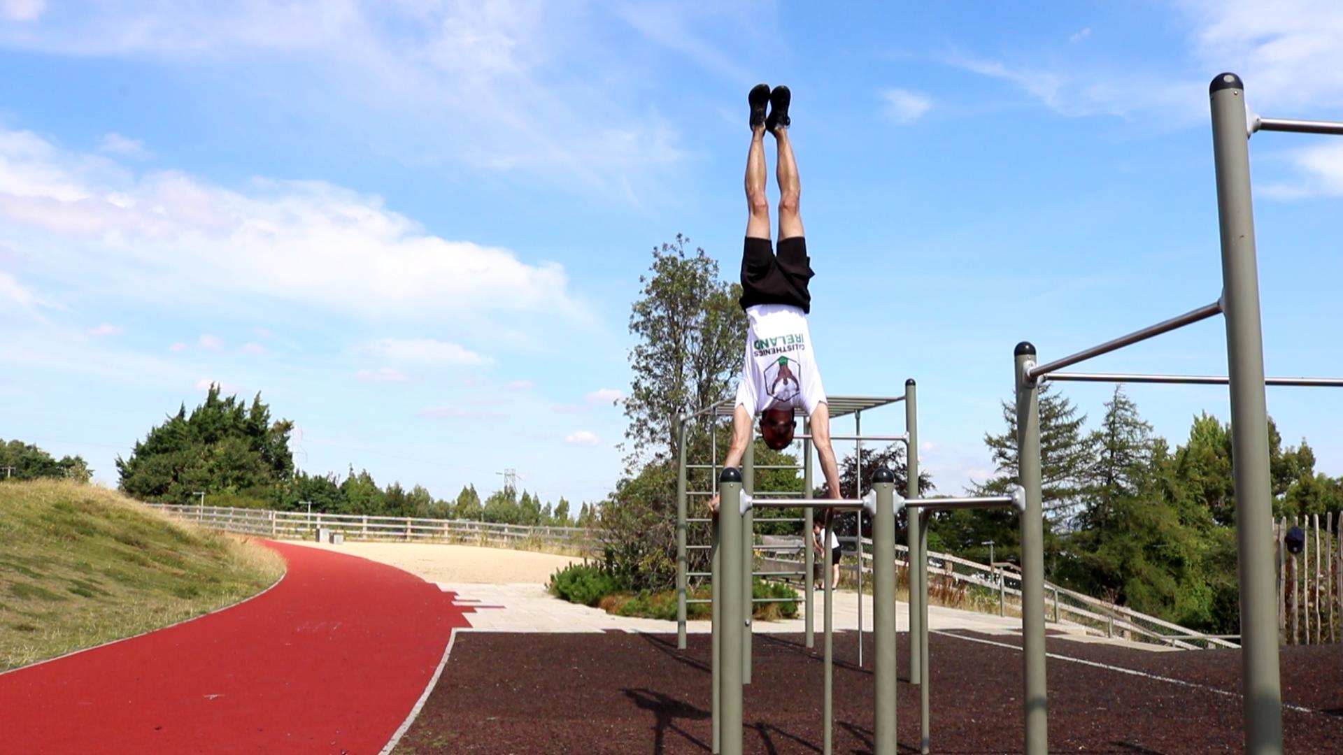 Handstand on dip bars at an outdoor calisthenics park in Ireland, showing the benefits of bodyweight training